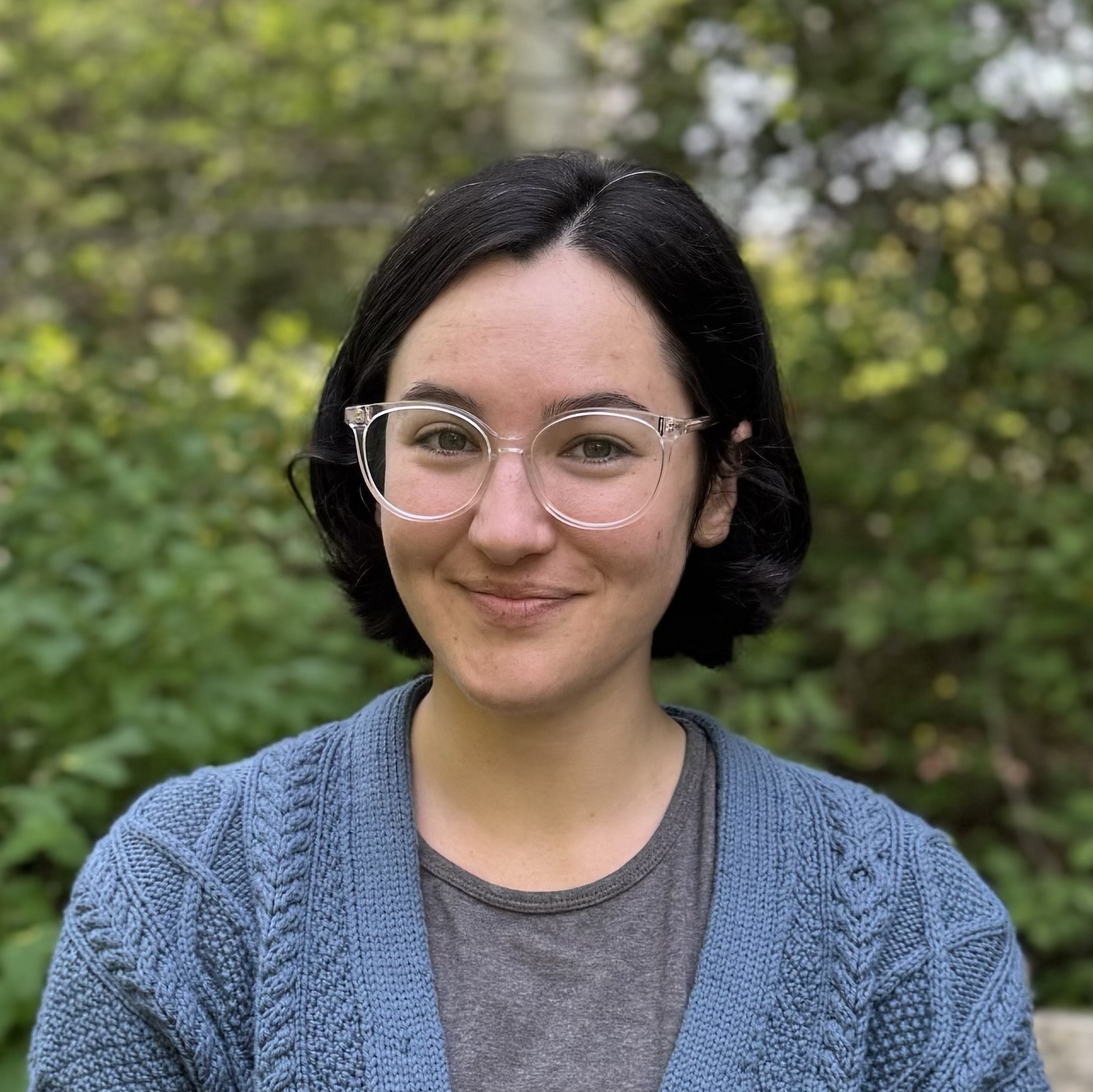 Cecilia Martindale smiles outside in front of greenery. She is wearing glasses and a grey t-shirt and blue cardigan.